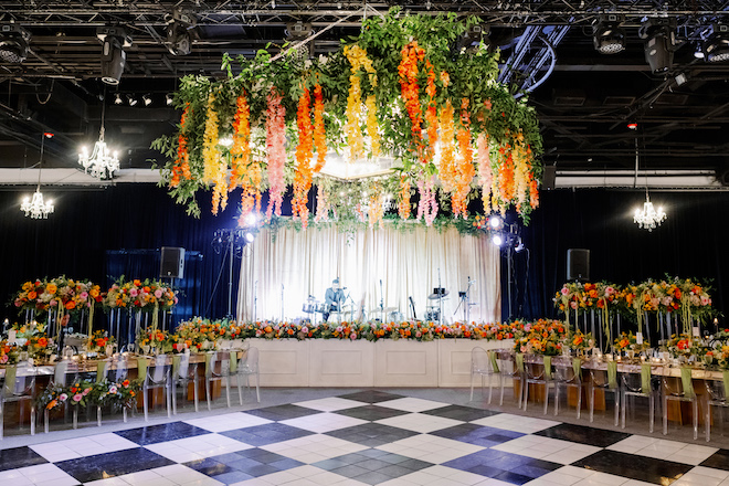 A black and white checkered dance floor with a orange, yellow and pink floral installation above it. 