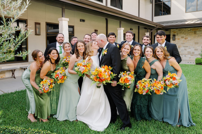 The bride and groom kissing with their wedding party smiling around them.