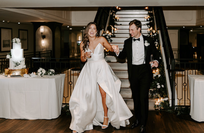 The bride and groom hold hands as they enter their winter wedding reception at the Magnolia Hotel Houston.