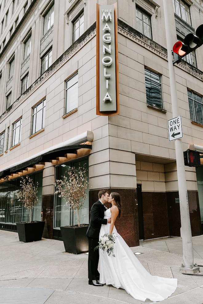 The bride and groom share a kiss outside of their wedding reception venue, the Magnolia Hotel Houston.