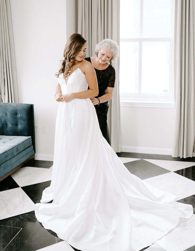 The mother of the bride helps the bride zip into her dress before her sophisticated winter wedding in Houston.