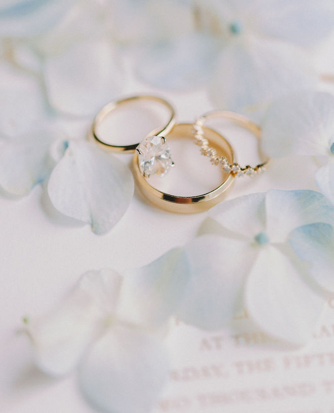 The bride and groom's wedding rings on an invitation with blue floral petals. 