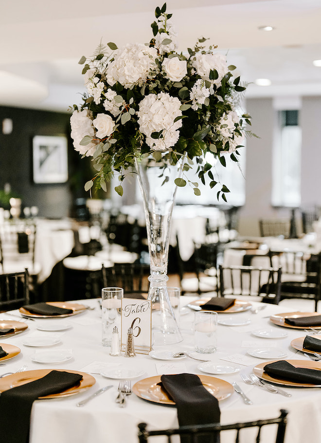 Tall white floral centerpieces and black linen napkins detail the reception all-white ballroom wedding. 