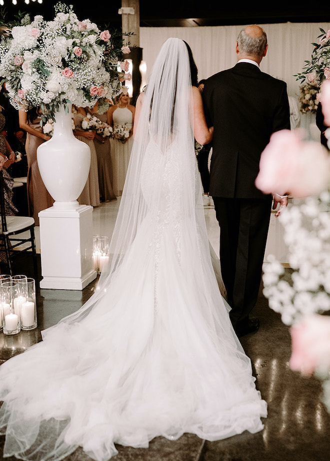 The father of the bride walks the bride down the aisle who is wearing a designer wedding gown by Ines di Santo. 