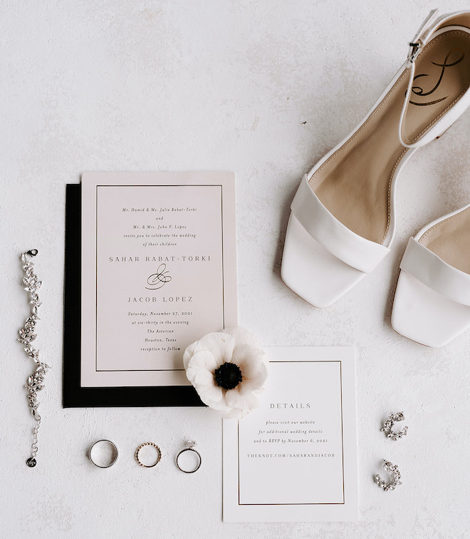 Jewelry, heeled shoes, a flower and a wedding invitation set against a black envelope 
