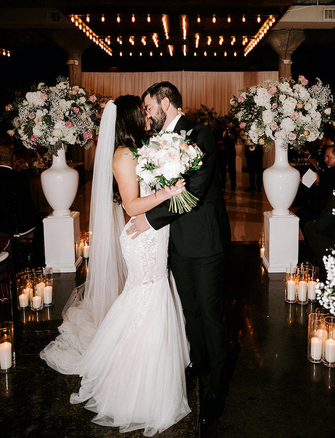 The bride and groom share a kiss in the aisle at their downtown Houston wedding venue, The Astorian. 