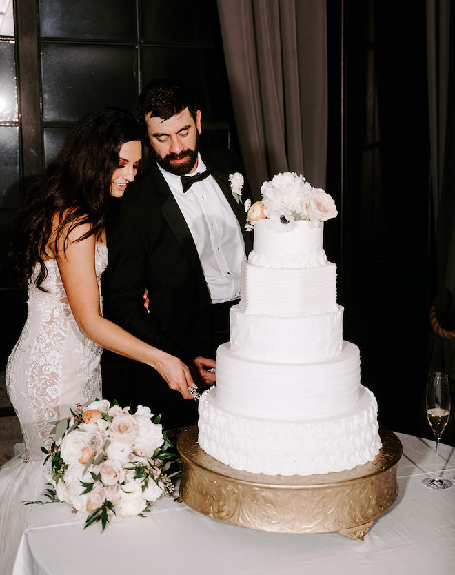 The bride and groom cut into their five-tier white wedding cake during their wedding reception. 