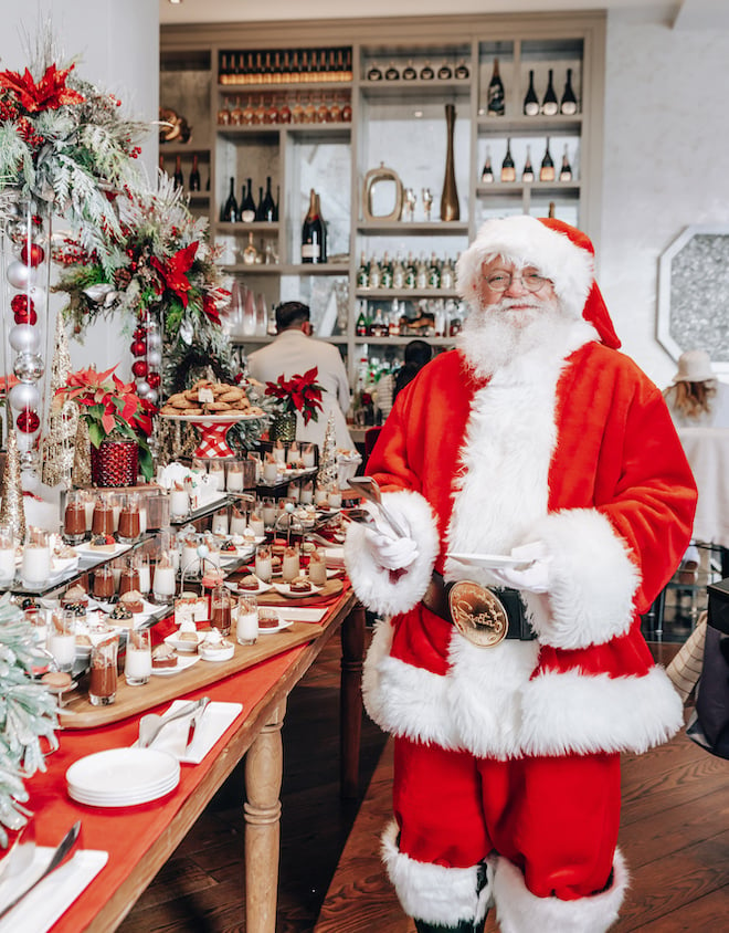A man dressed up as Santa Clause next to a table decorated with desserts and Christmas decorations at The Post Oak Hotel at Uptown Houston.