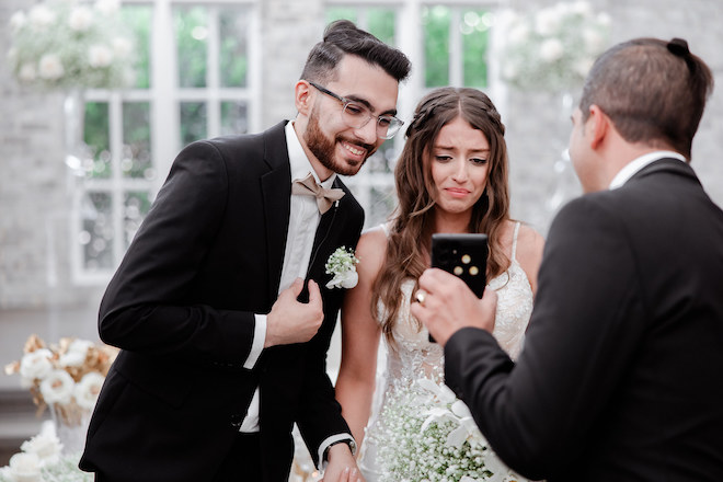 The bride and groom smiling at a phone in the ceremony space. 