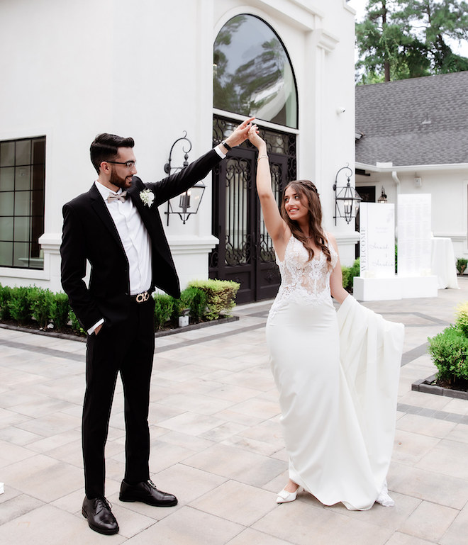 The bride and groom dancing in front of a white wedding venue.