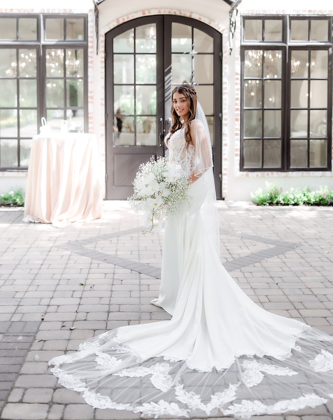 The bride posing in front of the wedding venue and a bouquet of baby's breath and white florals.