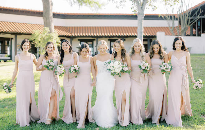 The bride and her bridesmaids walk holding hands outside at their Texas ranch wedding in Brenham, Texas.