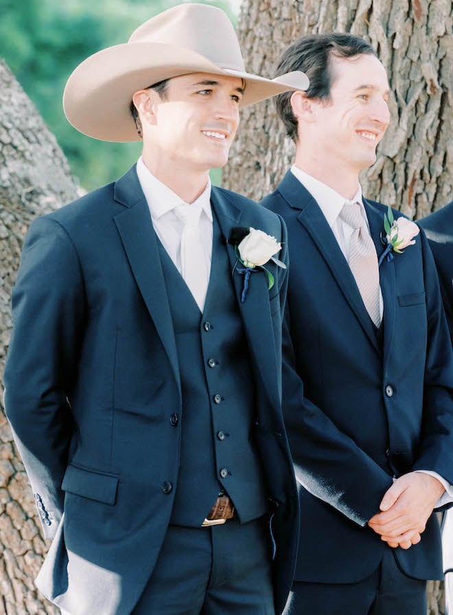 The groom smiles as his bride walks down the aisle at their outdoor wedding ceremony on a family Texas ranch.