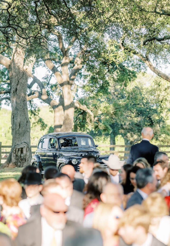 The bride pulls up to her wedding ceremony in a vintage black car. 