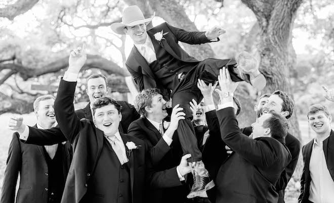 The groomsmen celebrate by holding the groom up on their shoulders for his wedding day. 