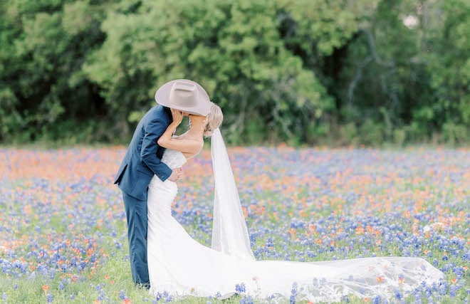 The bride and groom share a kiss in an open field of blue and orange wildflowers.