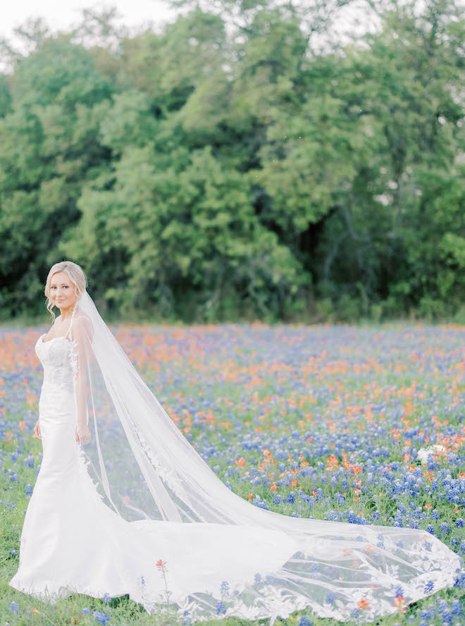 The bride poses in an open field of orange and blue wildflowers on family land in Brenham, Texas.