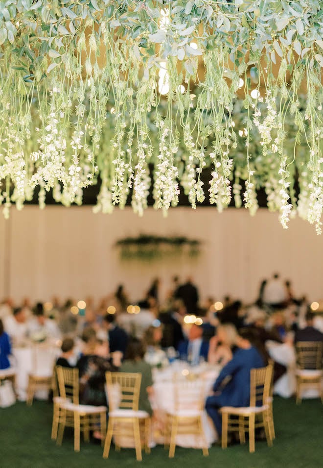 Greenery and small white florals hang from the chandeliers at the bride and groom's wedding reception.