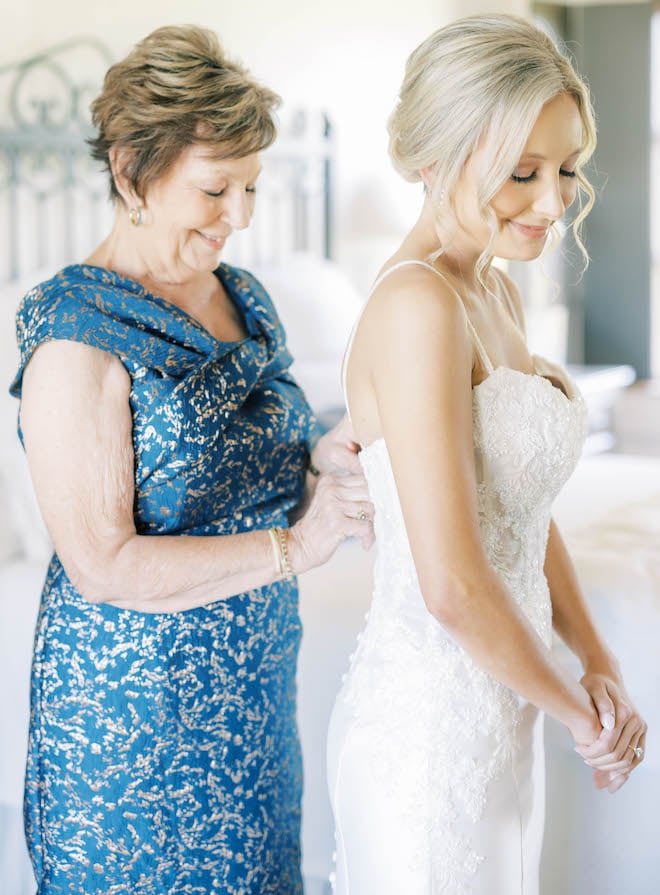 The mother of the bride zips the bride into her beaded wedding gown. 