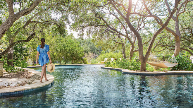 A lady walking along the ledge of a pool in the hill country. 