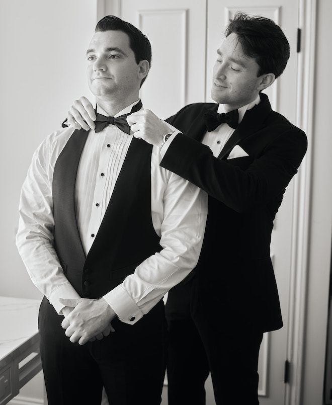 A groomsmen helping the groom put on his bowtie. 