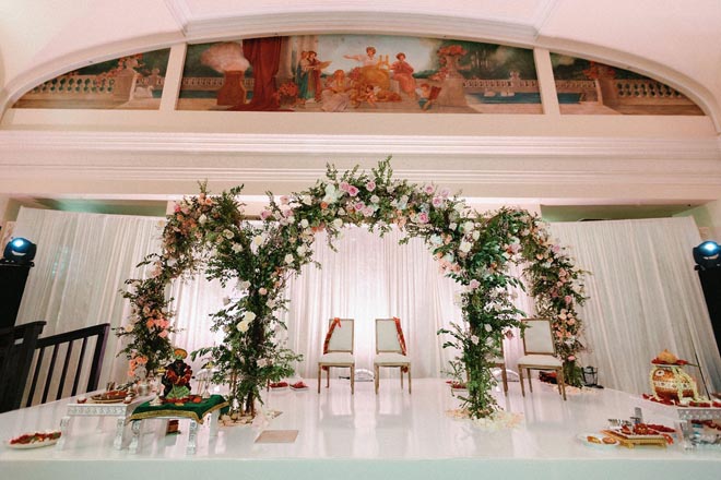 Floral arches with pink and white flowers decorate the alter at the Crystal Ballroom At The Rice in Downtown Houston.