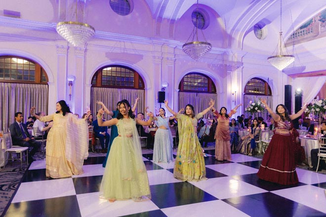 Wedding guests wearing traditional Indian clothing dance at the wedding reception.
