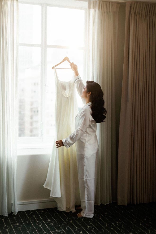 The bride holds up her white wedding gown in the bridal suite at the Magnolia Hotel Houston.