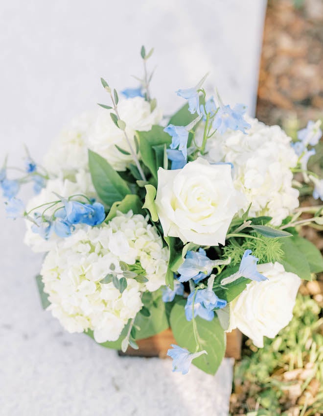 White roses and blue flowers detail the aisle at the outdoor wedding ceremony.