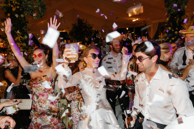 A bride and groom partying with their guests with confetti in the air. 