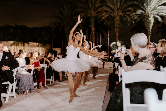 Ballerinas dancing down the aisle with guests on either side of them. 