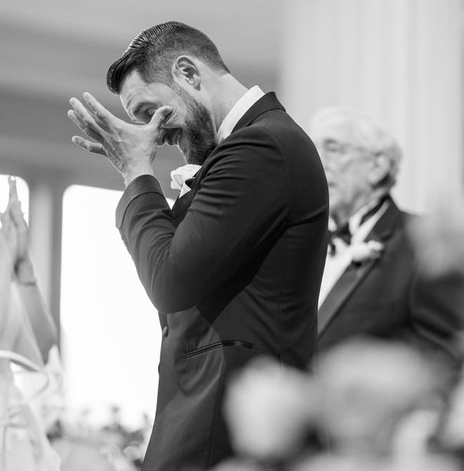 The groom wiping a tear from his eye at the altar. 