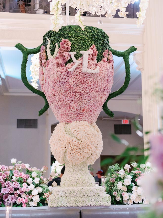 A large vase-shaped floral arrangement with neutral, pink and green florals and the couple's initials. 