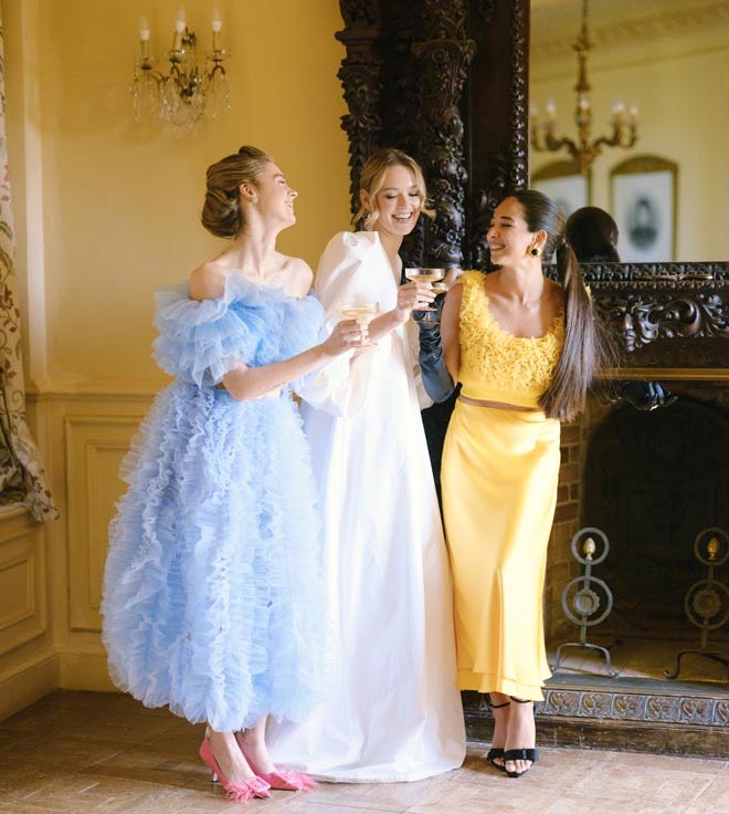The bride and her bridesmaids in colorful dresses laughing and holding champagne. 