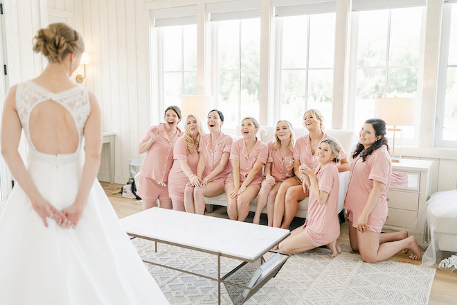 The bridesmaids in pink pajama sets seeing the bride for the first time in her wedding dress. 
