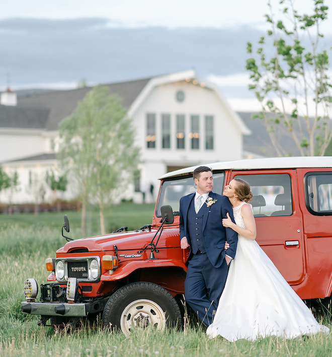 The bride and groom posing in front of a red vintage Toyota Land Cruiser. 