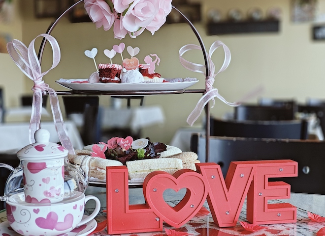 A pink, heart decorated tea cup, pastries and a red sign saying love decorate the table at McHughTea Room and Gifts. 