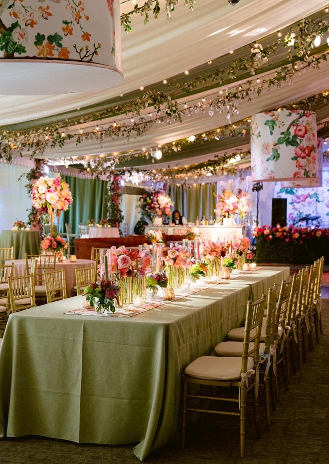 A long reception table with green linens and florals lining the center of the table. 