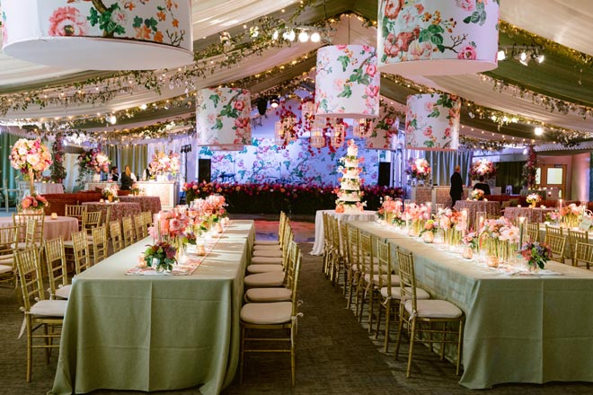 Long reception tables in green tablecloths with floral lanterns above them.