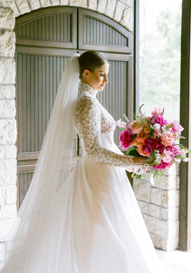 The bride wearing a lace and satin bridal gown holding her bouquet of pink flowers. 