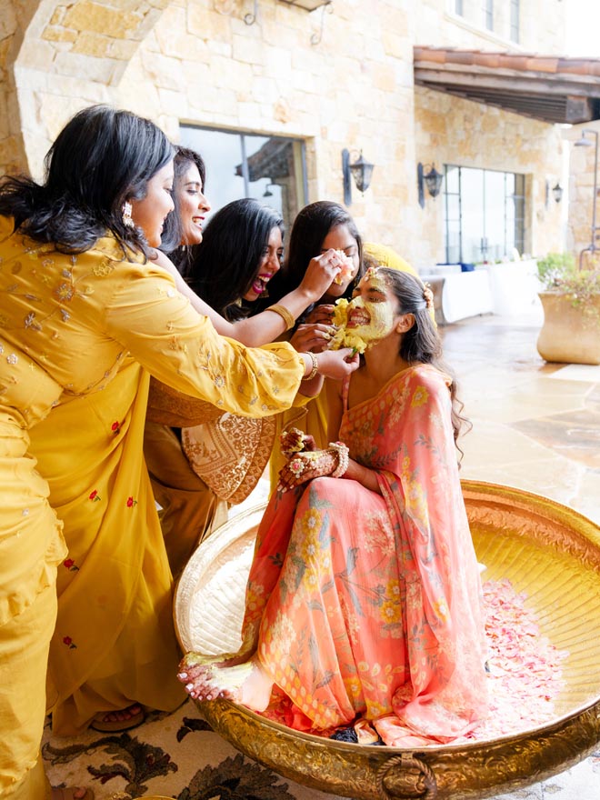 The bride's friends and family apply yellow turmeric paste to her face.