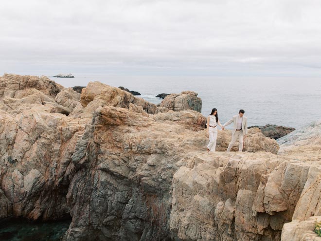 The couple hold hands as they walk across the rocks on the California coastline.