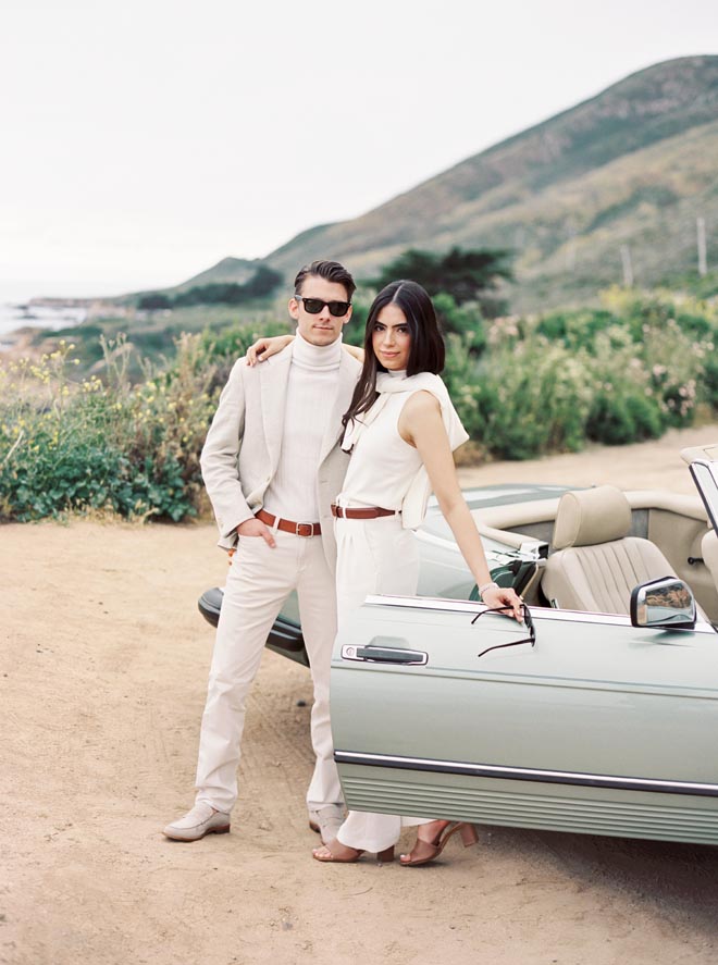 The couple stand beside an old Mercedes on the California coastline.