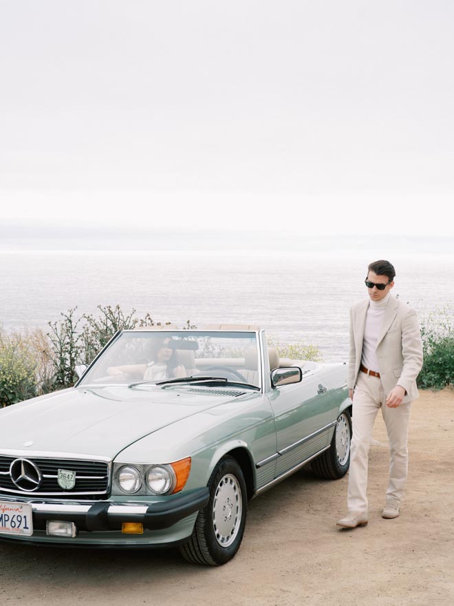 The man walks beside the vintage Mercedes along the coastline of Big Sur in California. 