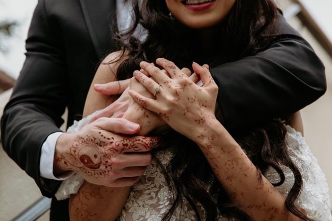 The bride and groom embrace with their hands detailed in Henna tattoos. 