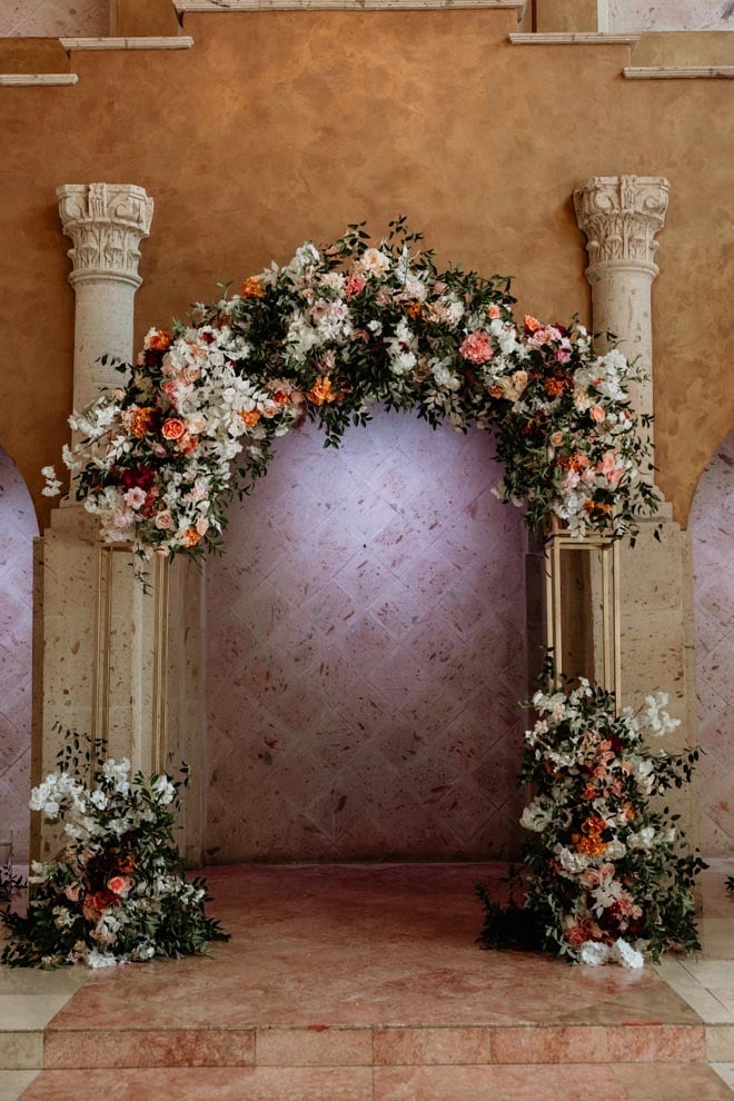A floral arch of white, peach, greenery and blush flowers decorate the wedding alter. 