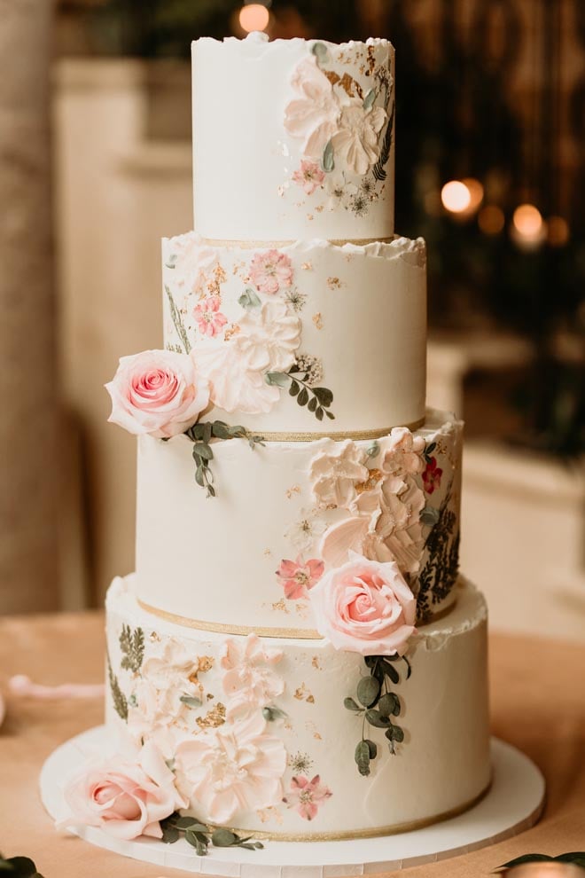 A 4-tier wedding wedding cake detailed in blush colored roses and flowers is served at the wedding reception.