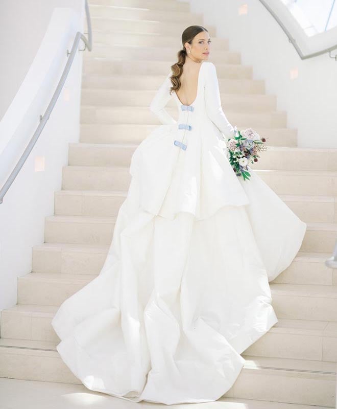 A bride wearing the "Last First Kiss" gown walking up the stairs holding a floral bouquet. 