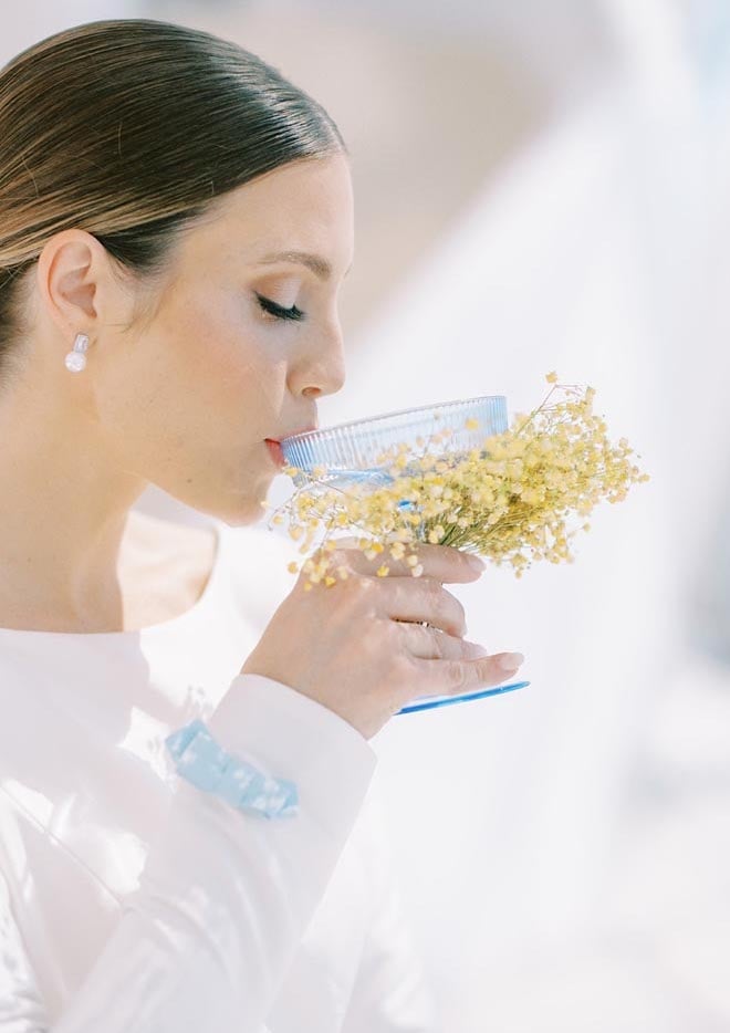 The bride sipping a blue glass with yellow flowers wrapped around it. 