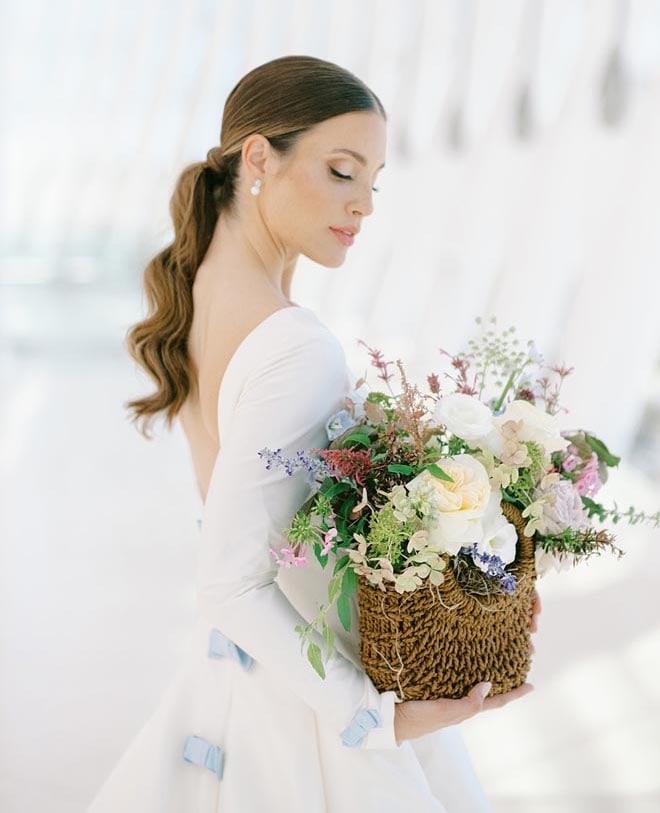 A bride wearing the "Last First Kiss" gown by Sareh Nouri and holding a basket of flowers. 